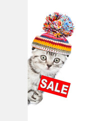 Aufkleber - Kitten wearing a warm hat holds sales symbol behind empty banner. isolated on white background
