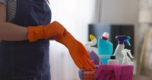  Person In Apron Putting On Orange Cleaning Gloves, With Supplies In Background