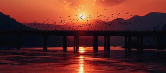 Wall Mural - Sunset silhouette of bridge, birds, and mountains in vertical shot.