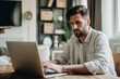 © Tymofii Borysenko - Man in a shirt sitting at the desk with laptop at home, freelancer working from home