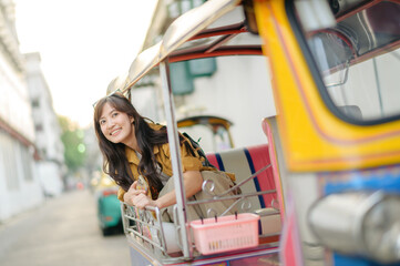 Wall Mural - Attractive beautiful tourist woman or traveler woman sitting on tuk tuk taxi exploring the city on summer vacations, Khao San Road walking street at Bangkok, Thailand.