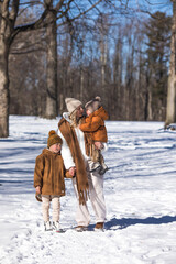 Winter weekend. Mother and two sons  in warm winterwear walking  while having fun in winter forest among trees