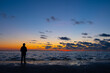 © Bjorn B - This tranquil image captures the silhouette of a lone individual standing on the shore, immersed in the serenity of the twilight. The horizon is painted with warm hues of orange and yellow, fading