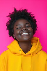 Wall Mural - A woman wearing a yellow hoodie smiles directly at the camera. This image can be used to depict happiness, positivity, or casual fashion