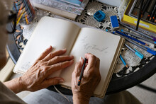 Elderly Hands Holding A Pencil And Writing On A Blank Page In A Notebook