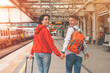 © Iryna - Happy loving couple with luggage and backpack walking along railway platform as they are ready to travel on holiday. Man and woman holding  hands,  looking back and smiling. Travel by train concept