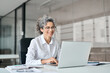 © insta_photos - Smiling mature business woman executive working in office using laptop. Happy professional senior middle aged female worker wearing glasses and white shirt using computer sitting at work desk.