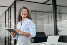 Smiling Mature Professional Business Woman Bank Manager, Older Happy Female Executive Or Lady Entrepreneur Holding Digital Tablet Pad Standing In Office At Work, Looking Away At Copy Space.