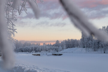 Frozen river and destroyed bridge, snow covered trees. Branches in blur. Day during the polar night in the Russian Far North.
