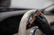 Car wash employee or a car detailing studio thoroughly cleans a light leather steering wheel with a brush and detergent