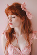 Pretty young red hair woman with freckles wearing coquette outfit with pink dress and bow. Side view portrait with eyes closed over pink background. Vertical image