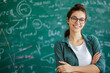 © Enigma - A smiling young woman with glasses standing in front of a chalkboard covered in math equations.