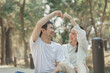 © kamiphotos - Happy young Asian couple in a park, Portrait of smiling couple near beautiful nature outdoors, lifestyle, Cheerful couple hugging each other, Young couple enjoying the sunny day at park