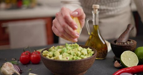 Wall Mural - Salsa recipe - Woman squeezes fresh lemon juice onto Chopped ingredients in s wooden bowl - avocado, onion and pepper