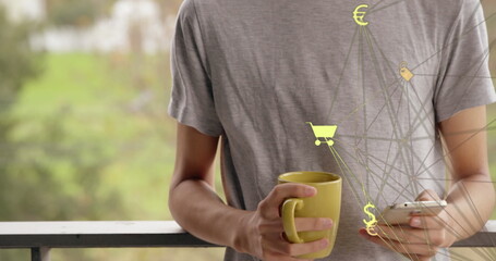 Poster - Globe of digital icons spinning against caucasian man with coffee cup using smartphone at home