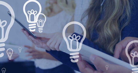 Poster - Light bulb icons floating against mid section of office colleagues using electronic devices