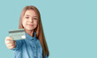 A girl in a denim shirt holds a credit card in her hands isolated on a blue background. Copy space