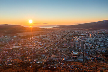 Wall Mural - Beautiful morning aerial view of the city. Top view of buildings and streets at sunrise. The sun rises over the sea bay. Travel to Siberia and the Russian Far East. Magadan, Magadan region, Russia.