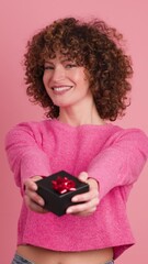 Wall Mural - Cheerful young woman giving gift box in pink studio. Vertical footage