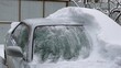 a gray car covered in snow and half cleared of snowdrift, the consequences for transport of a snow storm and a winter disaster with a blizzard and snowfall, cleaning a vehicle from fallen snow