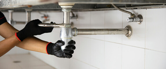 Wall Mural - Technician plumber using a wrench to repair a water pipe under the sink. Concept of maintenance, fix water plumbing leaks, replace the kitchen sink drain, cleaning clogged pipes is dirty or rusty.