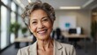 © Tom - Confident senior businesswoman, gray hair, professional attire, office setting, beaming smile, modern workplace.