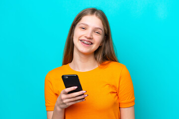 Wall Mural - Teenager Russian girl isolated on blue background using mobile phone