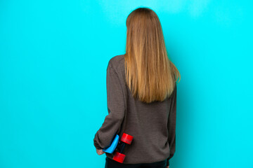 Wall Mural - Teenager Russian girl isolated on blue background with a skate in back position