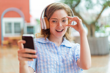 Poster - Young redhead girl headphones at outdoors making a selfie