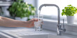 © Oleksandr - female hand holding a glass of water, kitchen faucet with white sink in the kitchen