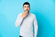 © luismolinero - Caucasian man over isolated blue background yawning and covering wide open mouth with hand