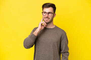 Wall Mural - Young caucasian man isolated on yellow background thinking an idea while looking up