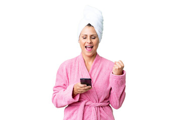 Canvas Print - Middle age caucasian woman in a bathrobe over isolated background with phone in victory position