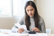 © KMPZZZ - Business financial concept, owe asian young woman sitting stressed, hand calculate expense, cost or budget on table at home from invoice or bill have no money to pay mortgage or loan, debt bankruptcy.