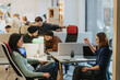 © qunica.com - A focused view of two women conversing in a bustling co working environment, with other creative professionals collaborating in the background. The modern workspace fosters teamwork and shared ideas.