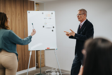 Wall Mural - Engaging image of a mature businessman leading a workshop while a female colleague presents at a whiteboard before an attentive audience.
