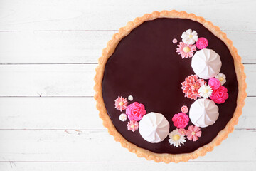 Poster - Gourmet chocolate tart with meringue and pink chocolate flowers. Top down view on a white wood background. Spring baking concept.