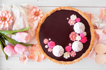 Poster - Gourmet chocolate tart with meringue and pink chocolate flowers. Overhead view table scene on a white wood background. Spring baking concept.