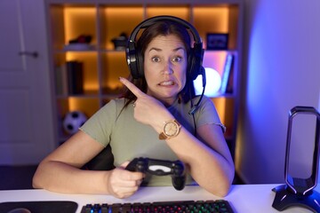 Wall Mural - Beautiful brunette woman playing video games wearing headphones pointing aside worried and nervous with forefinger, concerned and surprised expression