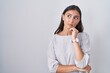 © Krakenimages.com - Young hispanic woman standing over white background with hand on chin thinking about question, pensive expression. smiling with thoughtful face. doubt concept.