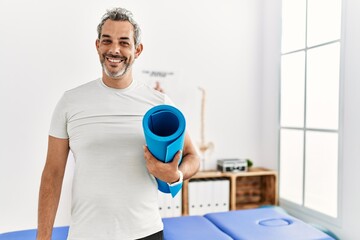 Poster - Middle age grey-haired man rehab patient holding yoga mat at rehab clinic