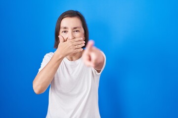 Poster - Middle age hispanic woman standing over blue background laughing at you, pointing finger to the camera with hand over mouth, shame expression