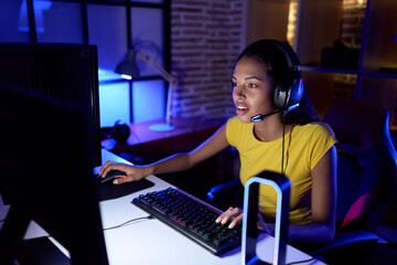 Canvas Print - Young african american woman streamer playing video game using computer at gaming room