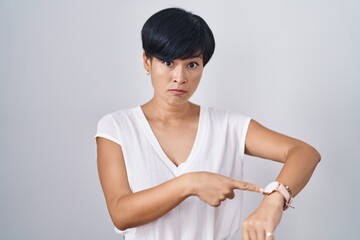 Wall Mural - Young asian woman with short hair standing over isolated background in hurry pointing to watch time, impatience, upset and angry for deadline delay