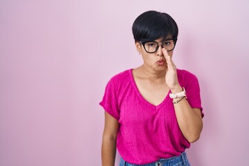 Wall Mural - Young asian woman with short hair standing over pink background hand on mouth telling secret rumor, whispering malicious talk conversation