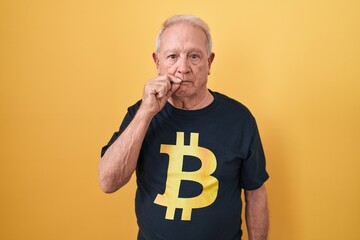 Wall Mural - Senior man with grey hair wearing bitcoin t shirt mouth and lips shut as zip with fingers. secret and silent, taboo talking