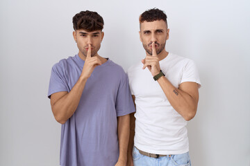 Poster - Homosexual gay couple standing over white background asking to be quiet with finger on lips. silence and secret concept.