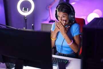 Wall Mural - Brunette young woman playing video games shocked covering mouth with hands for mistake. secret concept.