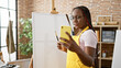© Krakenimages.com - Confident african american woman artist with braids skillfully drawing on canvas, smiling as she gives a painting lesson during a video call in art studio.