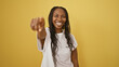 Smiling african american woman with curly hair pointing at camera, isolated on yellow background